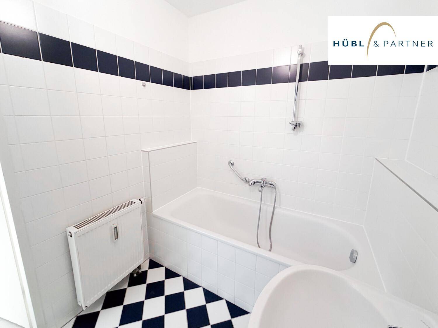 Badezimmer mit Badewanne, Heizkörper und schwarz-weiß kariertem Fliesenboden.
