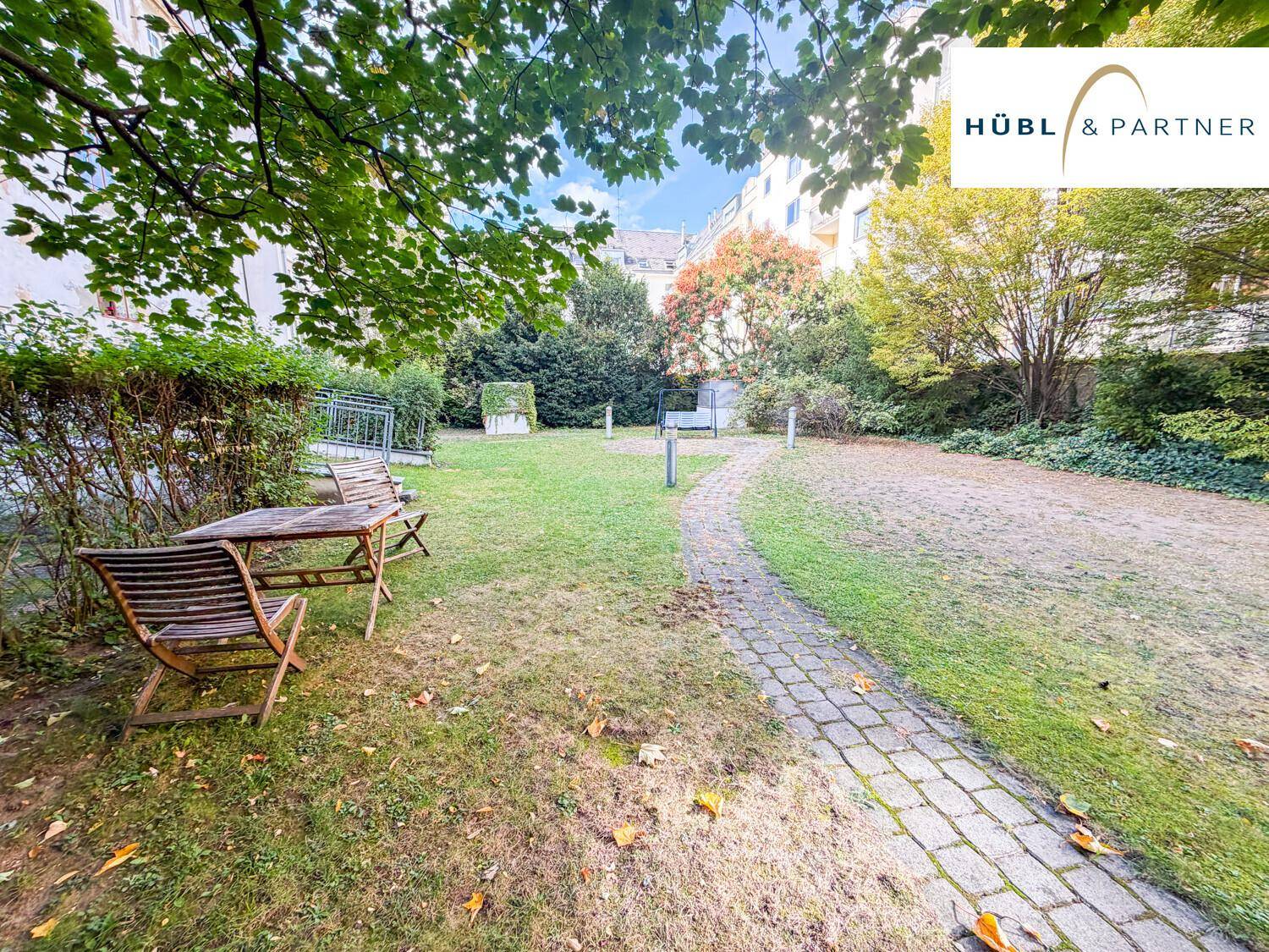 Gepflegter Gemeinschaftsgarten mit Rasenfläche und Holztisch mit Stühlen für gemütliche Stunden.