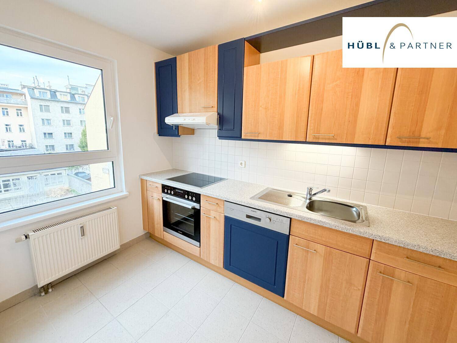 Funktionale Küche mit blauen und holzfarbenen Schränken, ausgestattet mit modernen Geräten und Fenster.