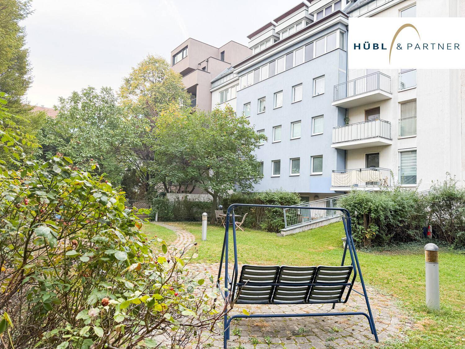 Grüner Gemeinschaftsgarten mit Schaukelbank und Bäumen, umgeben von Wohngebäuden.