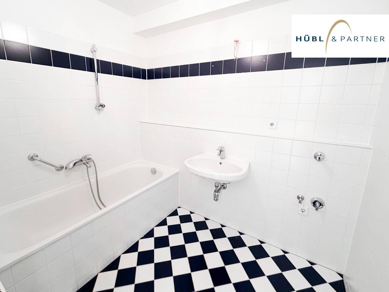 Badezimmer mit Badewanne, Waschbecken und markantem schwarz-weiß kariertem Fliesenboden.
