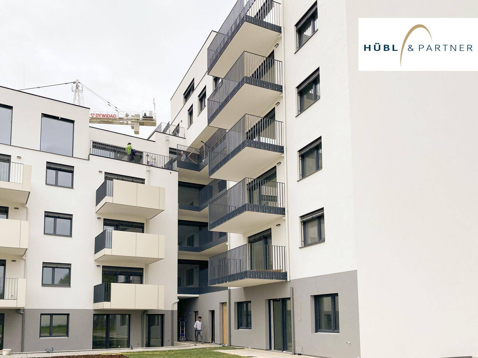 Moderne Wohnanlage mit mehreren Balkonen und einer Baustelle im Hintergrund.