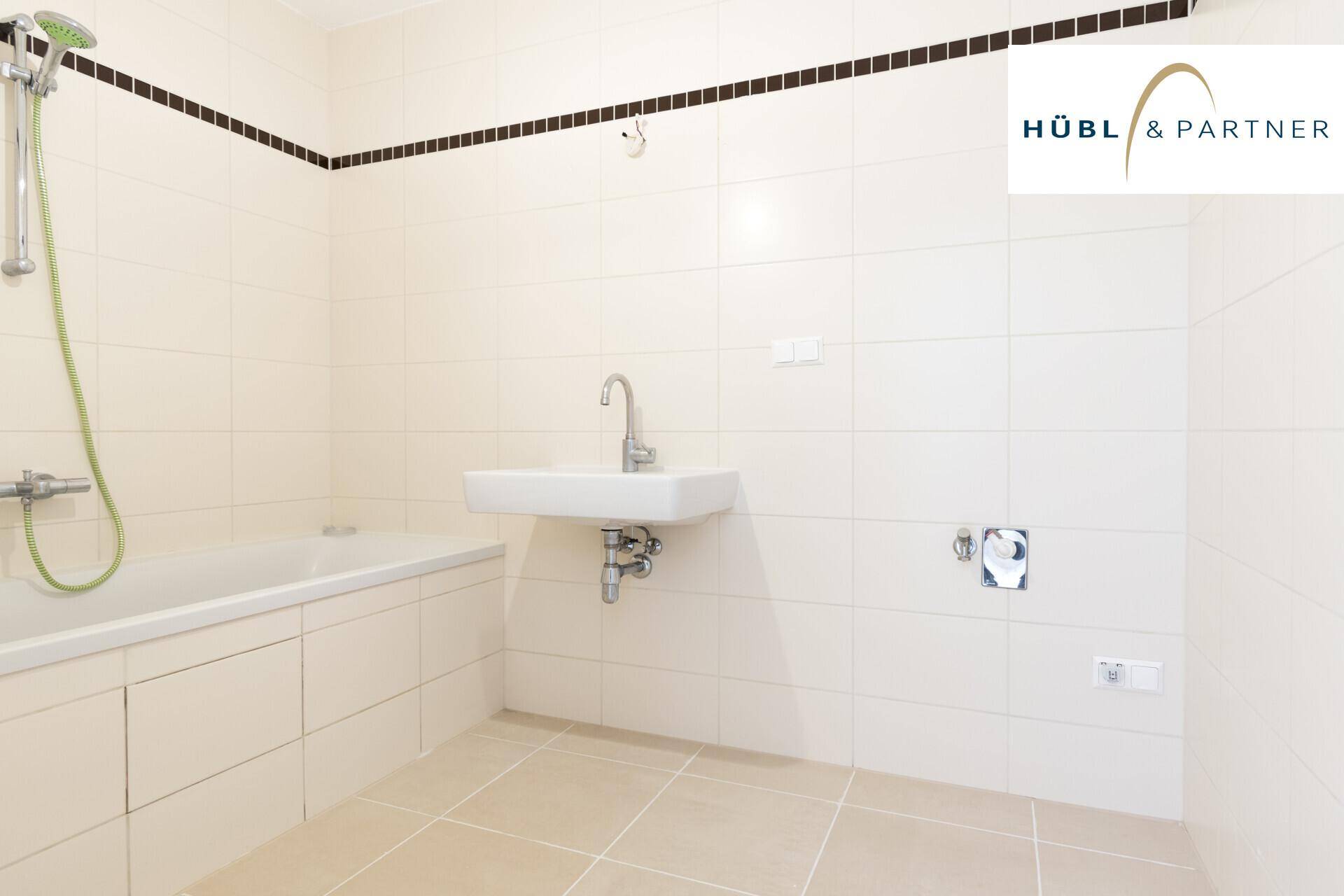 Helles Badezimmer mit beigefarbenen Fliesen, einer Badewanne mit Duschfunktion und einem Wandwaschbecken.