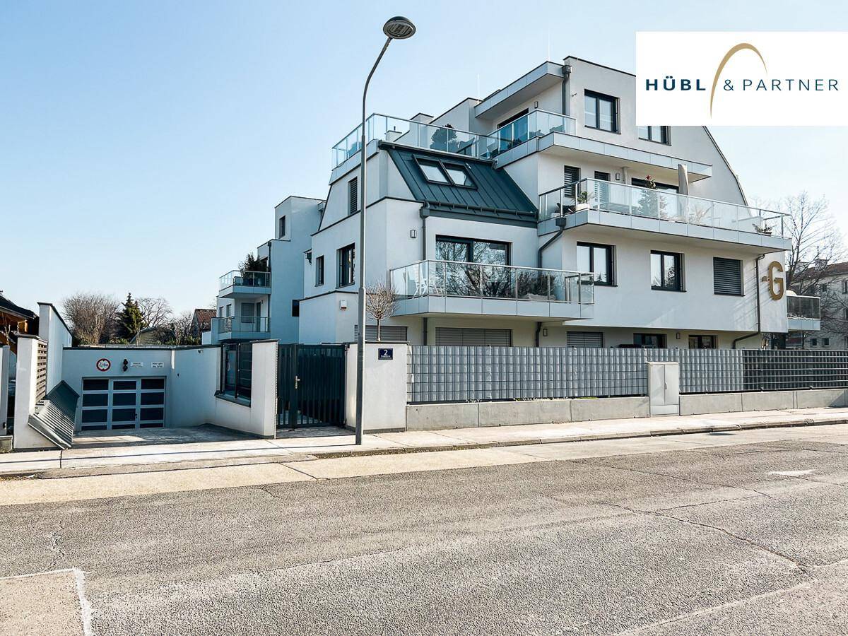 Moderne Wohnanlage mit mehreren Balkonen, Glasgeländern und Tiefgarageneinfahrt von der Straße.