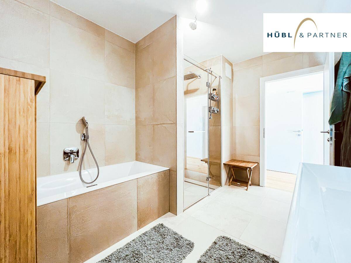 Helles Badezimmer mit beigefarbenen Fliesen, Badewanne und Duschvorrichtung.