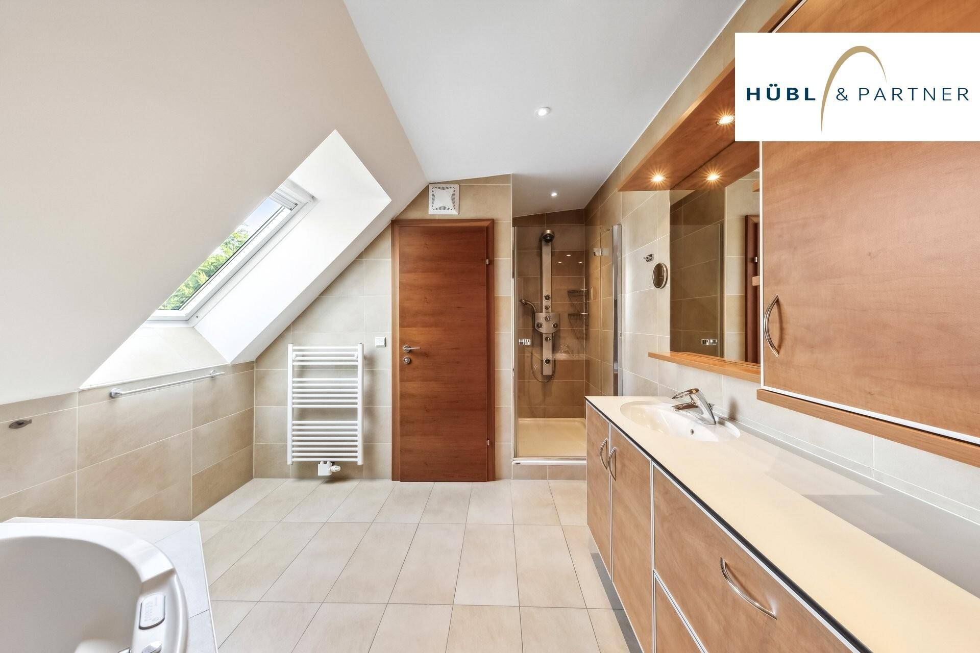 Modernes Badezimmer im Dachgeschoss mit Badewanne, Dusche und Dachfenster.
