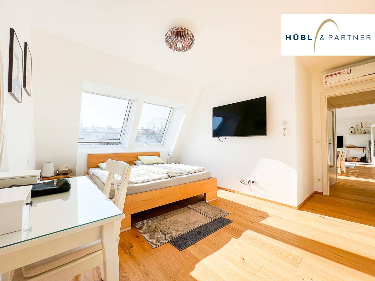 Helles Schlafzimmer mit Holzboden, Doppelbett, Schreibtisch und schrägen Dachfenstern.