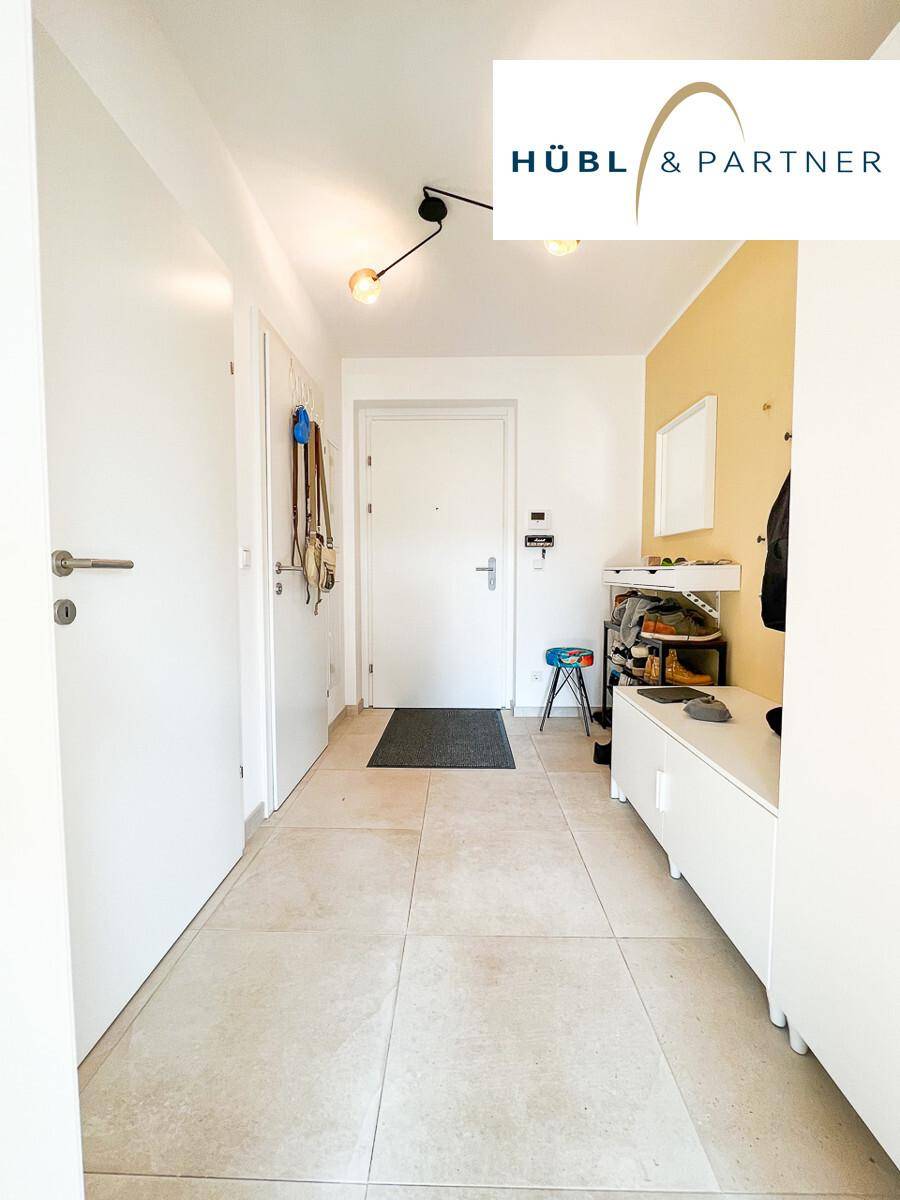 Freundlicher Eingangsbereich mit hellen Fliesen, gelber Akzentwand und praktischer Garderobe.
