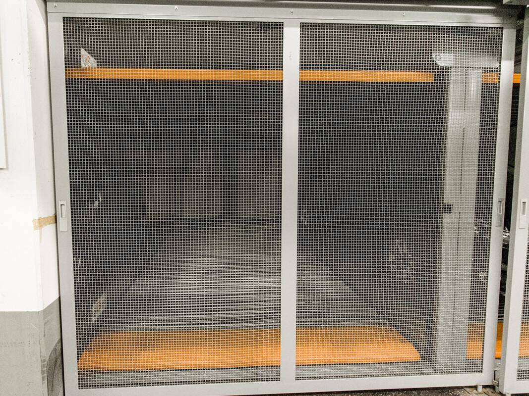 Abstellraum mit Metallgittertür und orangefarbenen Regalböden in einem Kellerbereich.