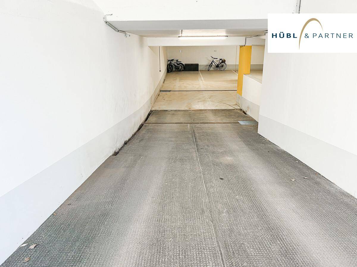 Einfahrt zu einer Tiefgarage mit Rampe und weiß gestrichenen Wänden.