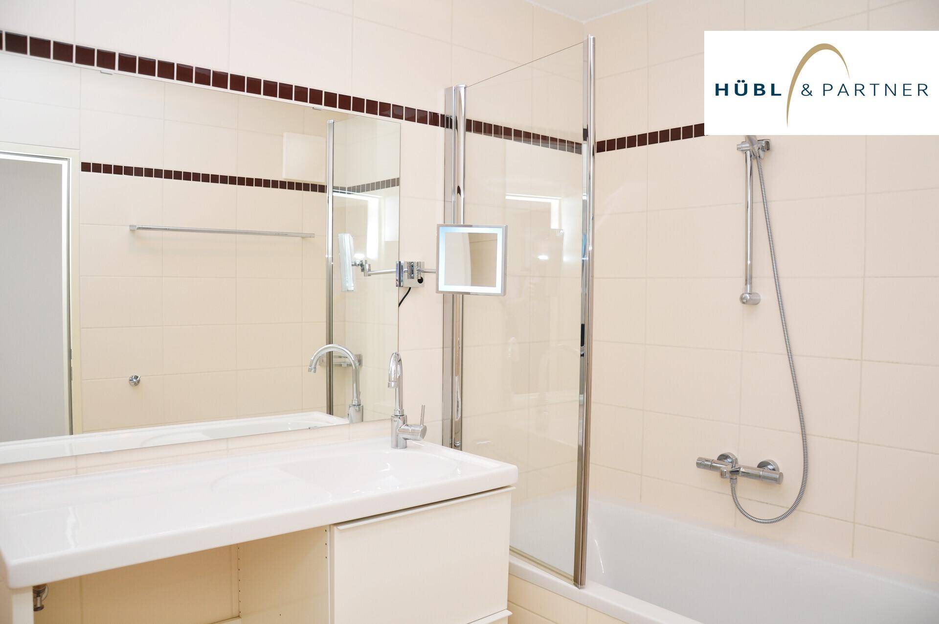 Modernes Badezimmer mit beigefarbenen Fliesen, Badewanne mit Duschwand und einem einzelnen Waschbecken.