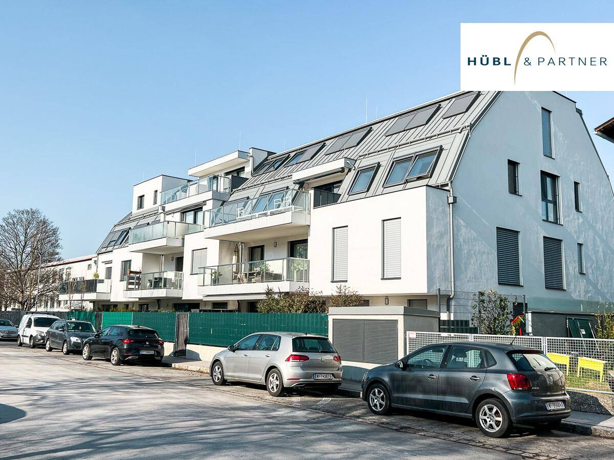 Moderne Wohnanlage mit weißer Fassade, Balkonen und Schrägdach an einer Straße.