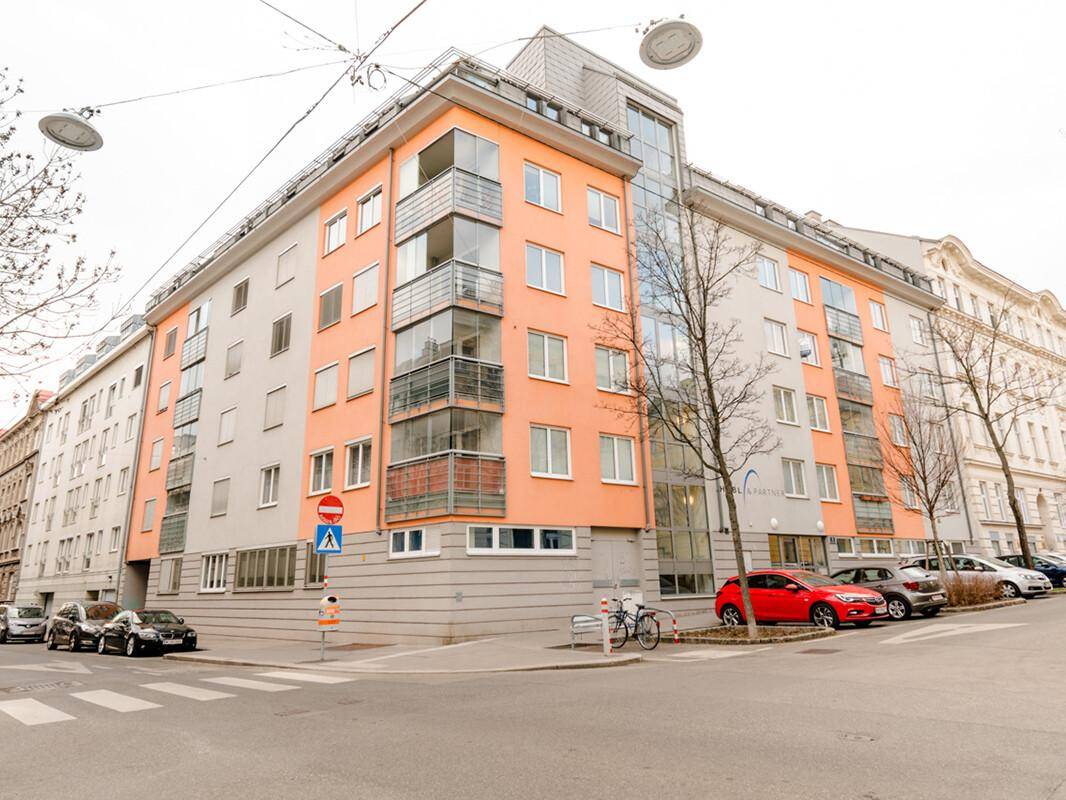 Modernes Mehrfamilienhaus mit orangefarbenen Akzenten und Balkonen an einer Stadtstraße.