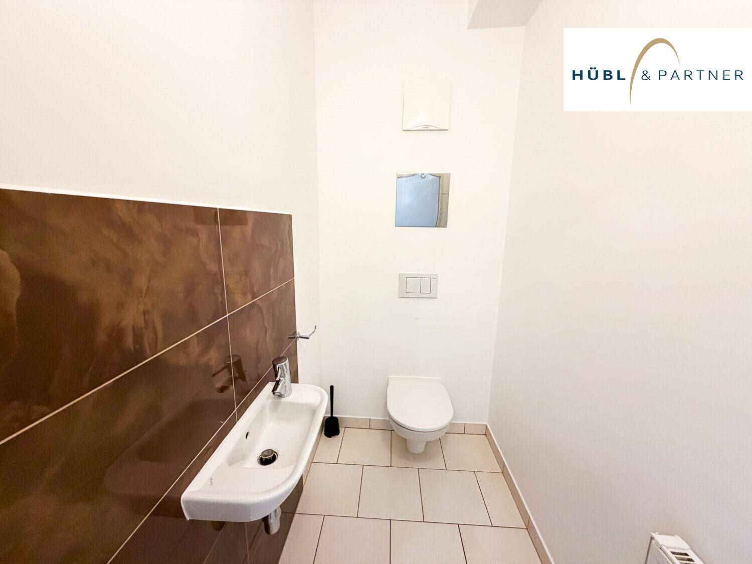 Modernes Gäste-WC mit wandhängender Toilette und kleinem Waschbecken, teilweise gefliest.
