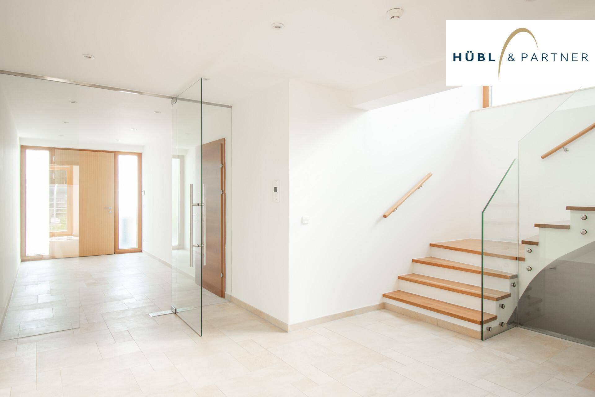Heller Eingangsbereich mit moderner Treppe aus Holz und Glas sowie Fliesenboden.