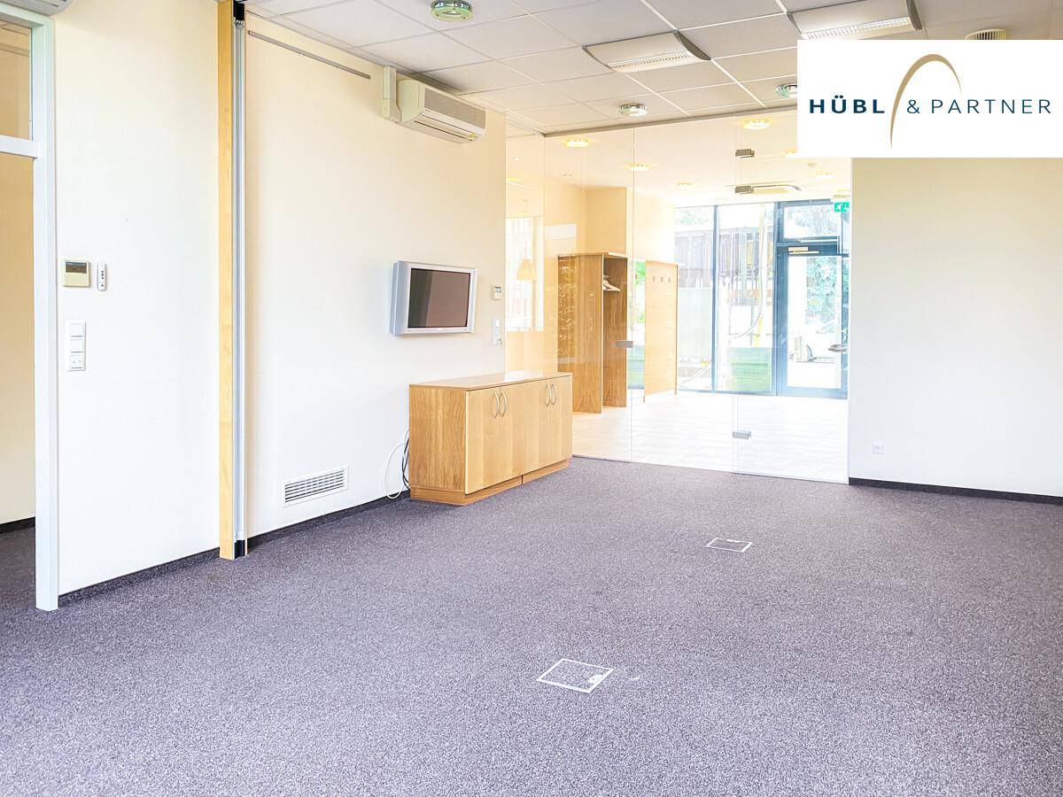 Geräumiger Büroraum mit Teppichboden, Klimaanlage und einem Sideboard, das zu einem weiteren Bereich führt.