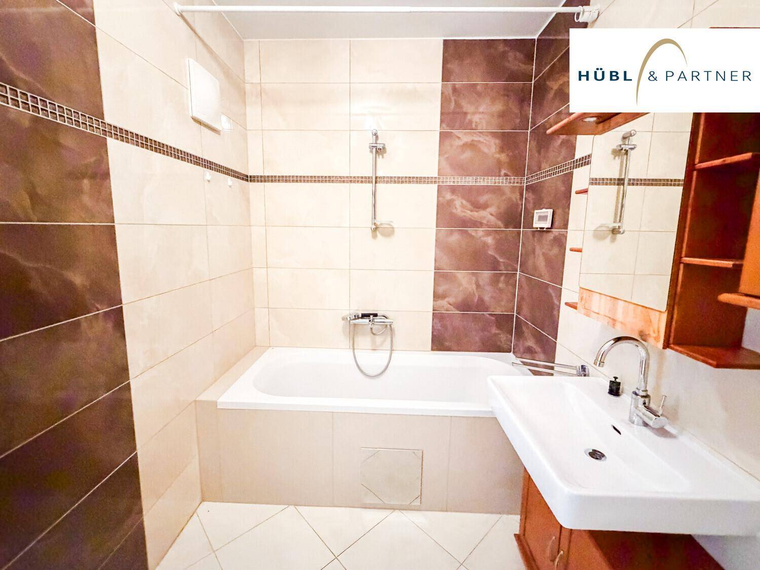 Helles Badezimmer mit Badewanne, Duscharmatur und Einzelwaschbecken, komplett gefliest.