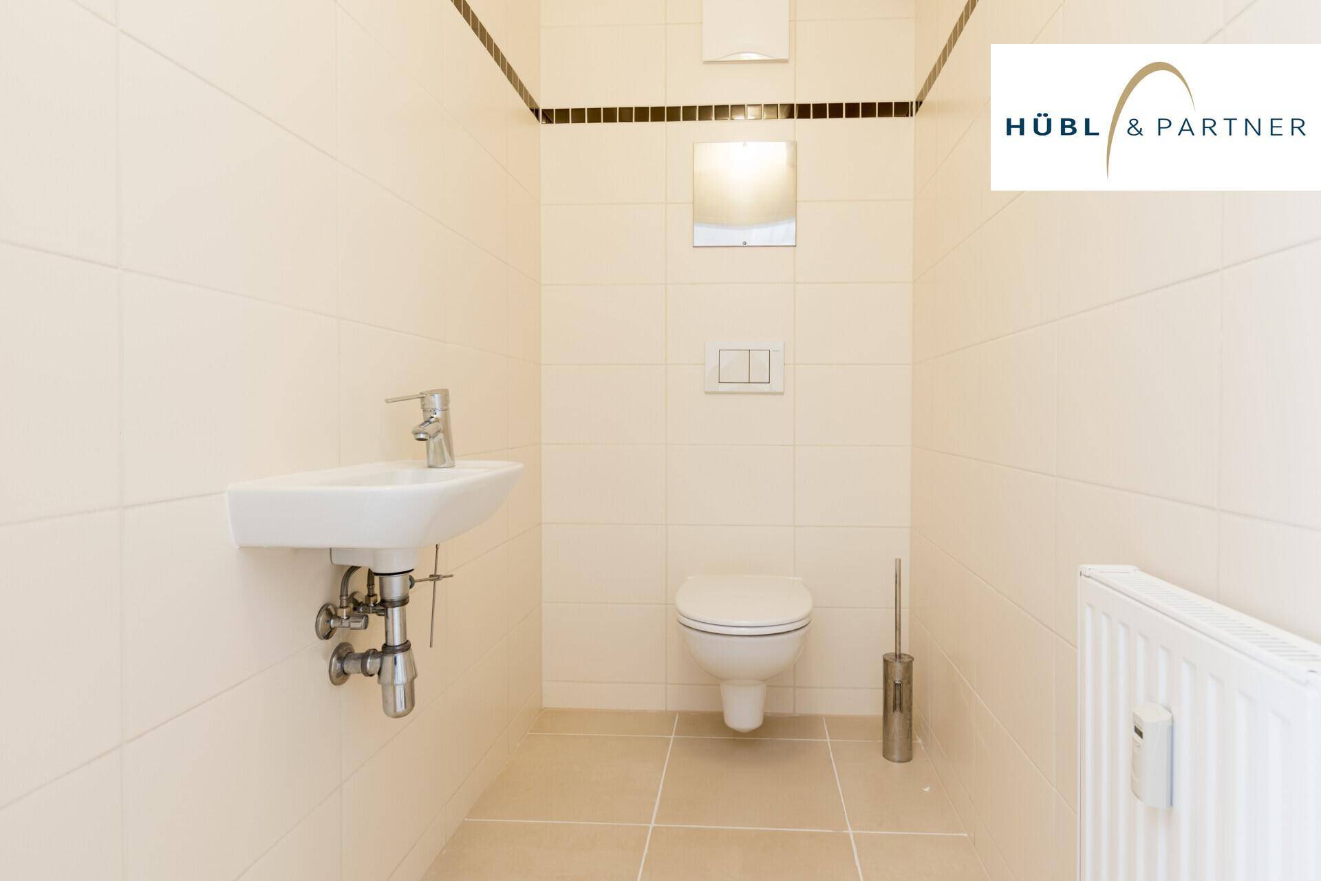 Separates WC mit beigefarbenen Fliesen, wandhängender Toilette und kleinem Handwaschbecken.