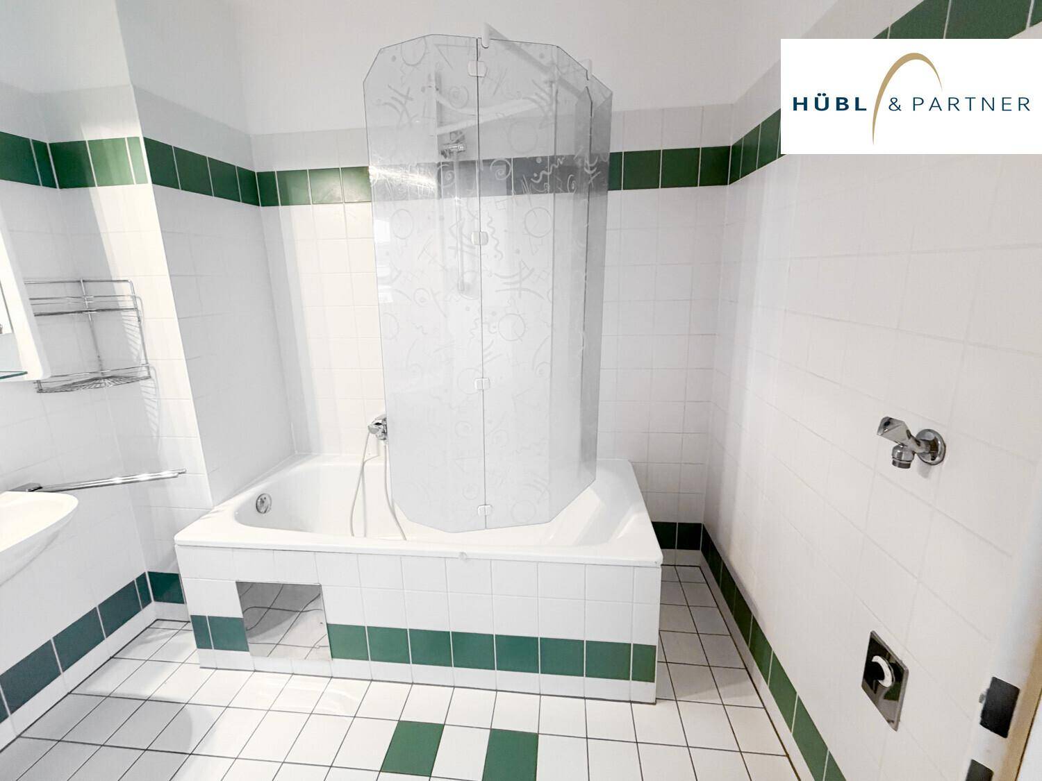 Badezimmer mit Badewanne, Duschabtrennung und charakteristischen grün-weißen Fliesen.