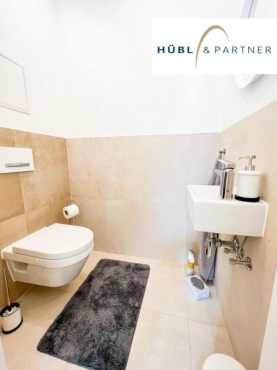 Helles Gäste-WC mit beigefarbenen Fliesen, wandhängendem WC und modernem Waschbecken.