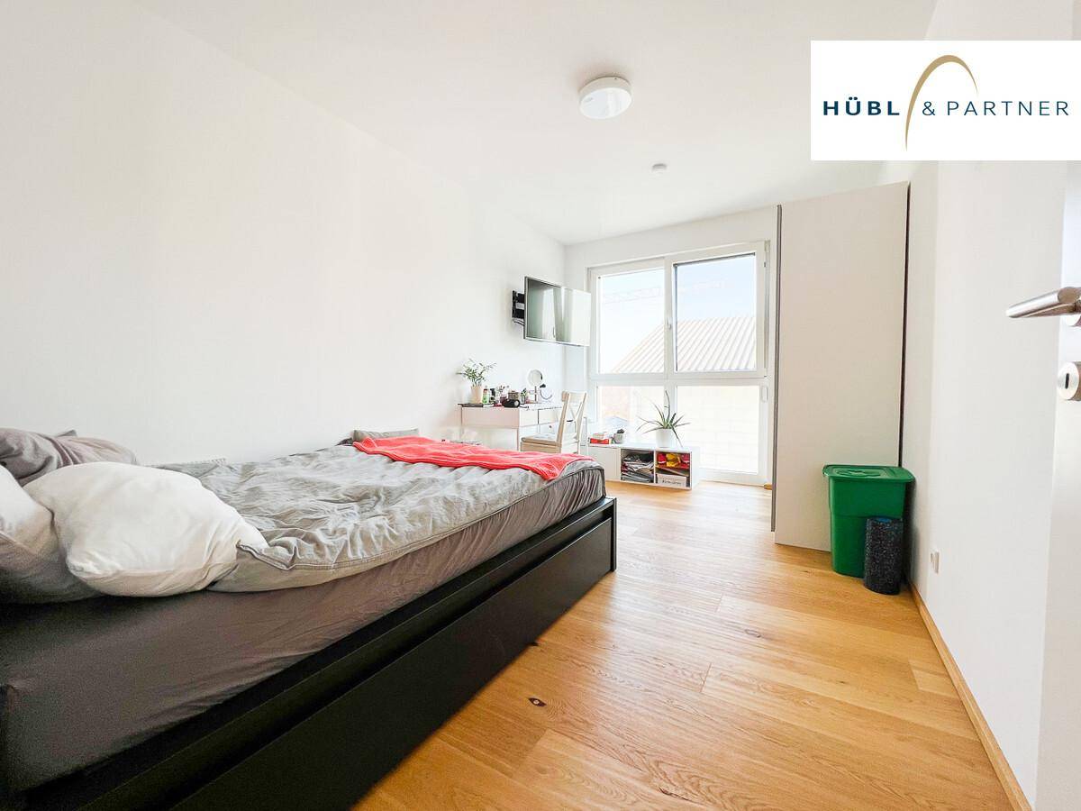 Helles Schlafzimmer mit Holzboden, Einzelbett, Schreibtisch und großem Fenster.