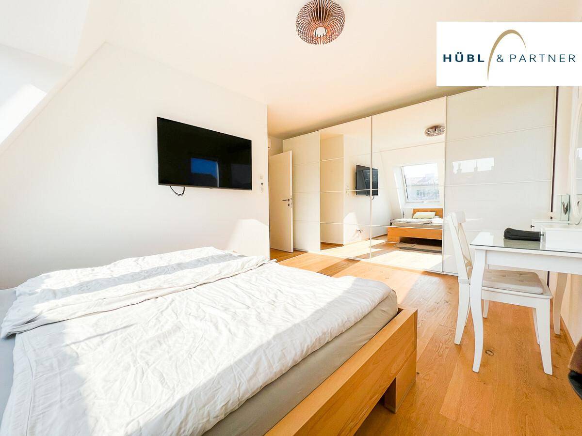 Schlafzimmer mit Holzboden, Doppelbett, großem Spiegelschrank und Schreibtisch.