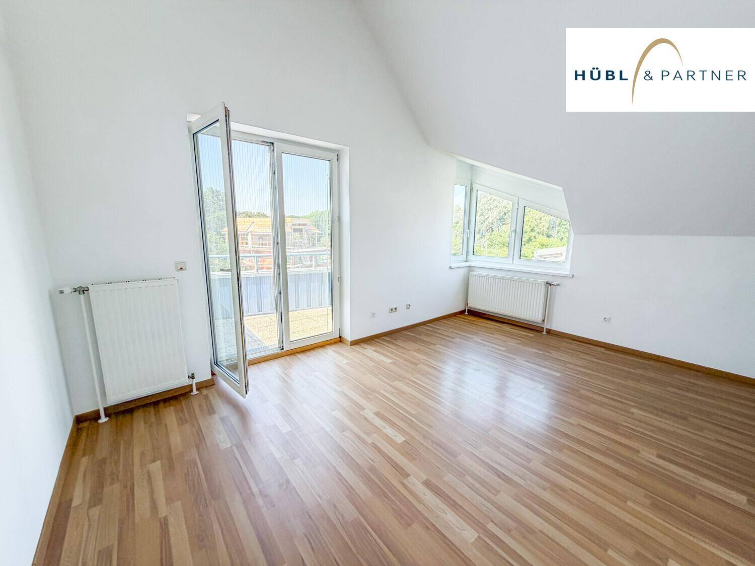 Geräumiger Wohnbereich im Dachgeschoss mit Holzboden und großen Fenstern zum Balkon.