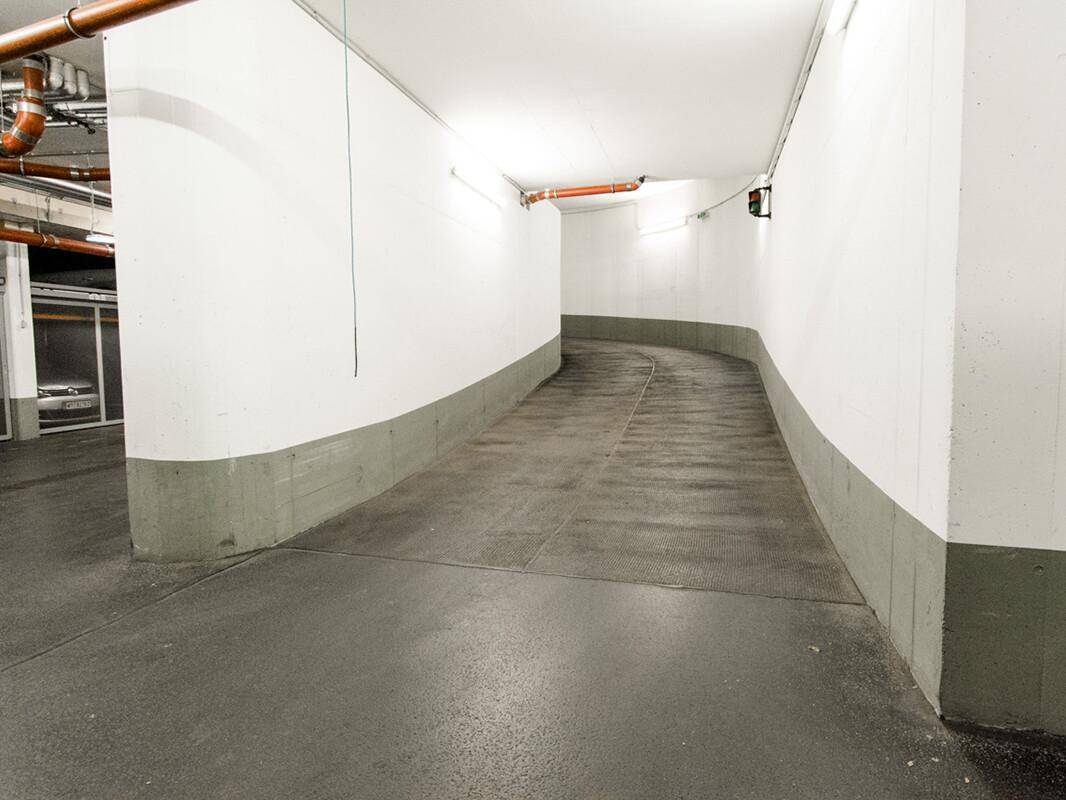 Zufahrtsrampe in einer Tiefgarage mit Betonboden und weißen Wänden, gut beleuchtet.