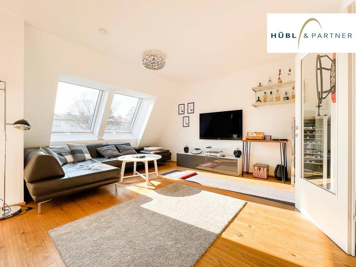 Gemütliches Wohnzimmer mit Holzboden, großem Sofa, Fernseher und schrägen Dachfenstern.