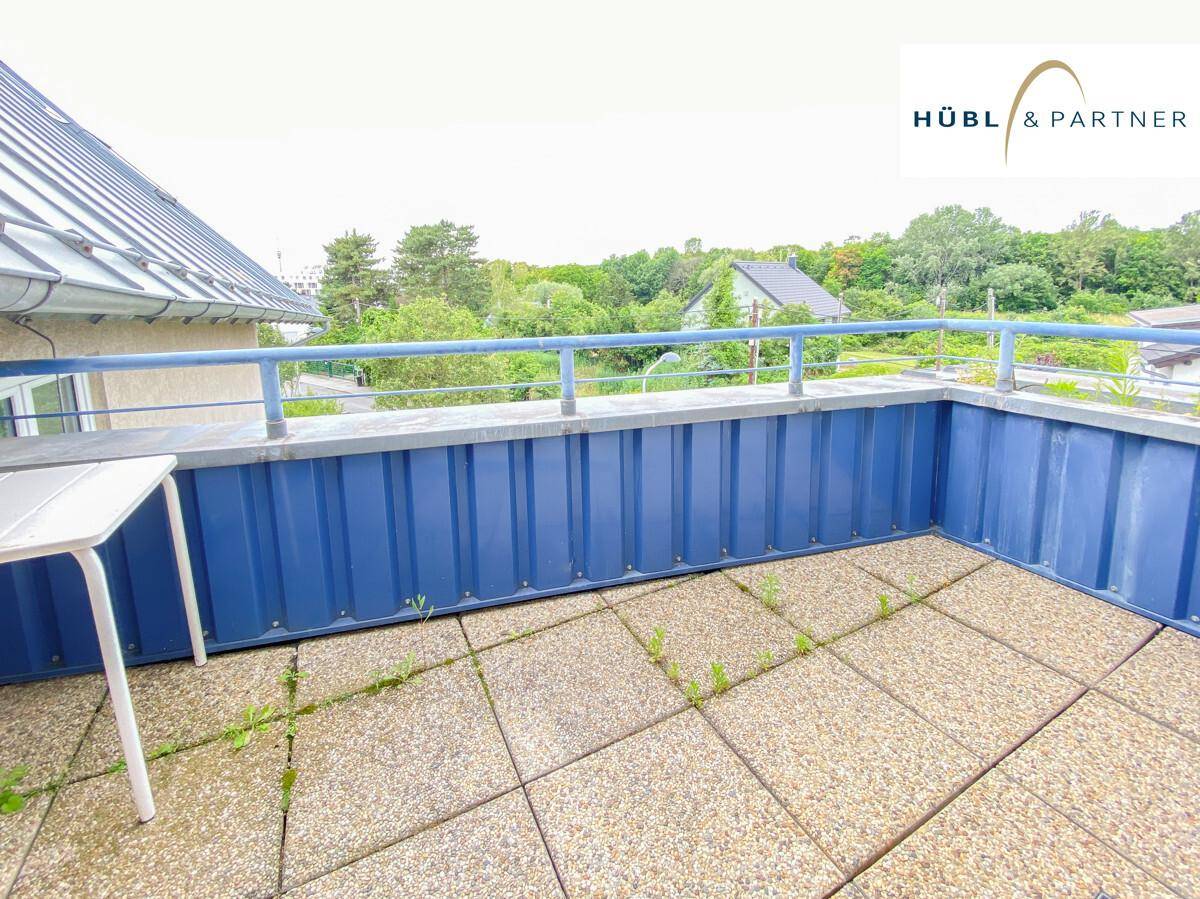 Geräumiger Balkon mit Fliesenboden und blauer Brüstung, umgeben von viel Grün.