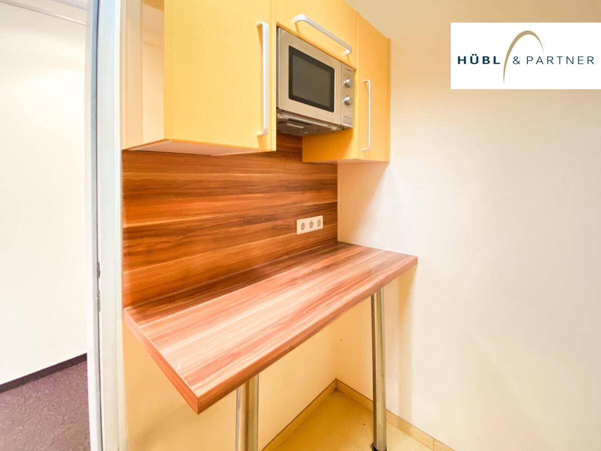 Kleine Küchenzeile mit Mikrowelle, gelben Oberschränken und einem ausklappbaren Holztisch.