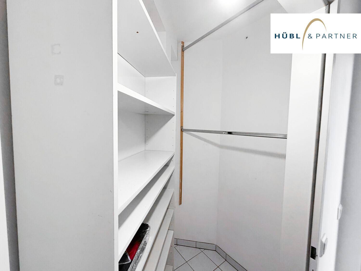 Praktischer begehbarer Kleiderschrank mit weißen Regalen und Kleiderstange auf Fliesenboden.