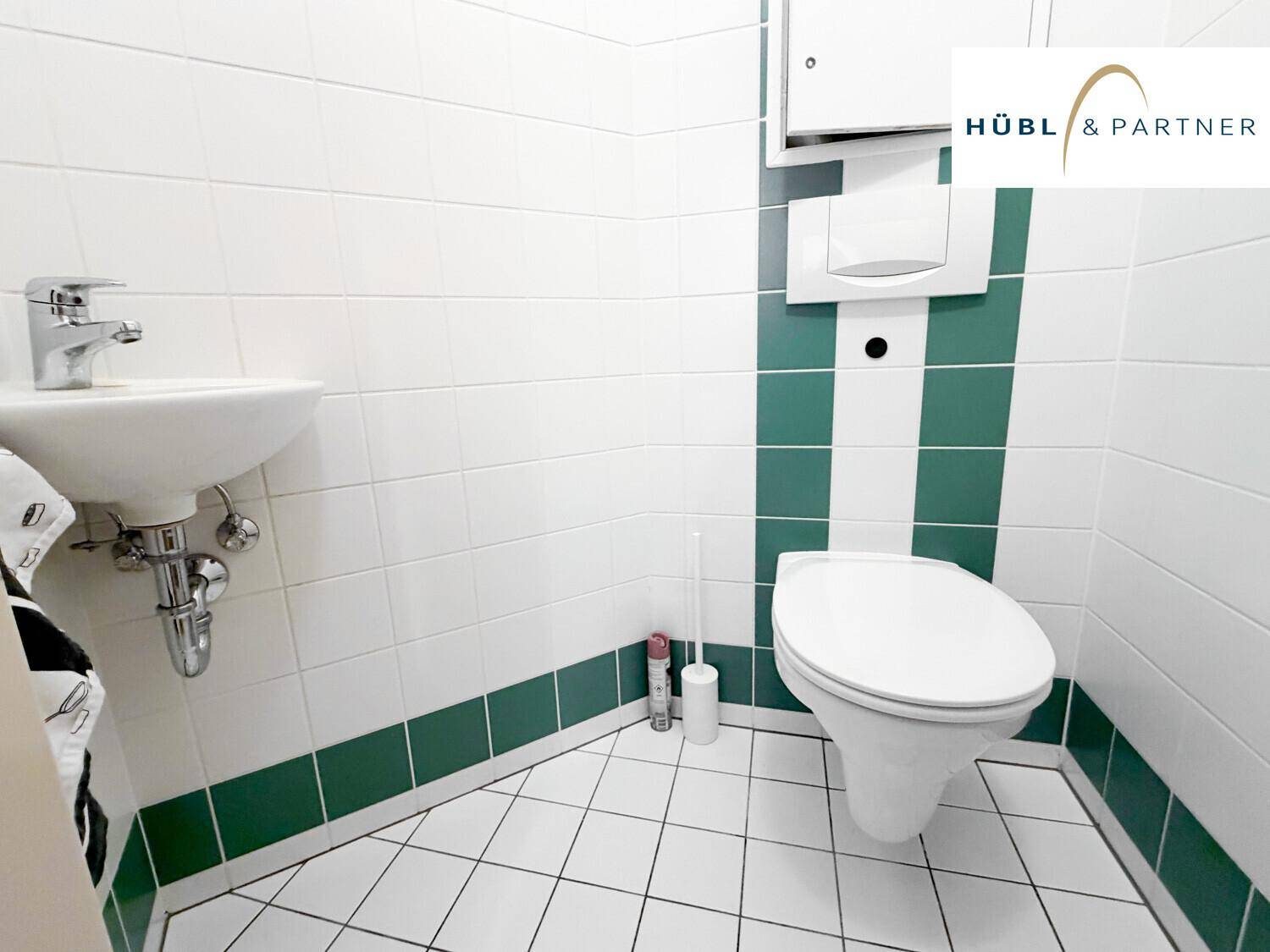 Kleines Gäste-WC mit wandhängender Toilette, Waschbecken und grün-weißen Fliesen.