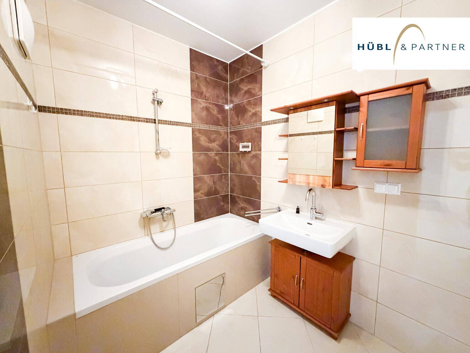Gefliestes Badezimmer mit Badewanne, Dusche, Einzelwaschbecken und Spiegelschrank in warmen Farbtönen.