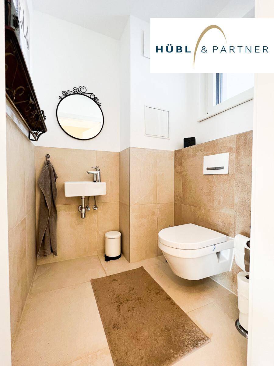 Modernes Gäste-WC mit beigefarbenen Fliesen, wandhängendem WC und kleinem Waschbecken.