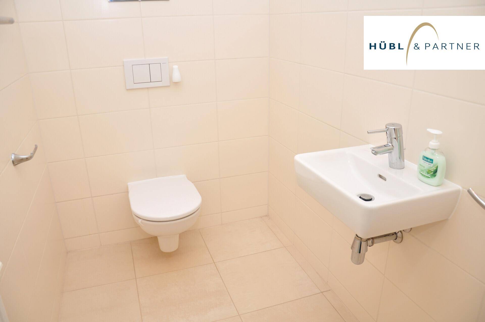 Separates WC mit beigefarbenen Fliesen, wandhängender Toilette und kleinem Handwaschbecken, sehr gepflegt.