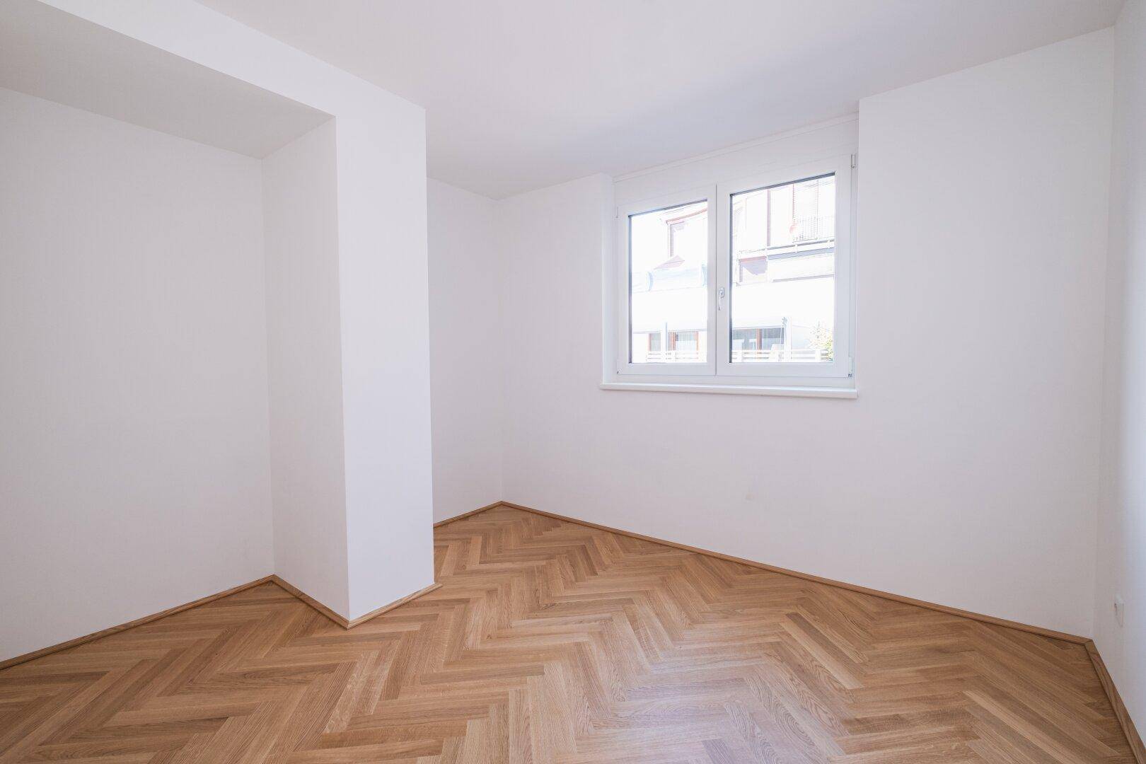 Gemütliches Zimmer mit Fischgrätparkett und einem Fenster mit Blick ins Grüne.