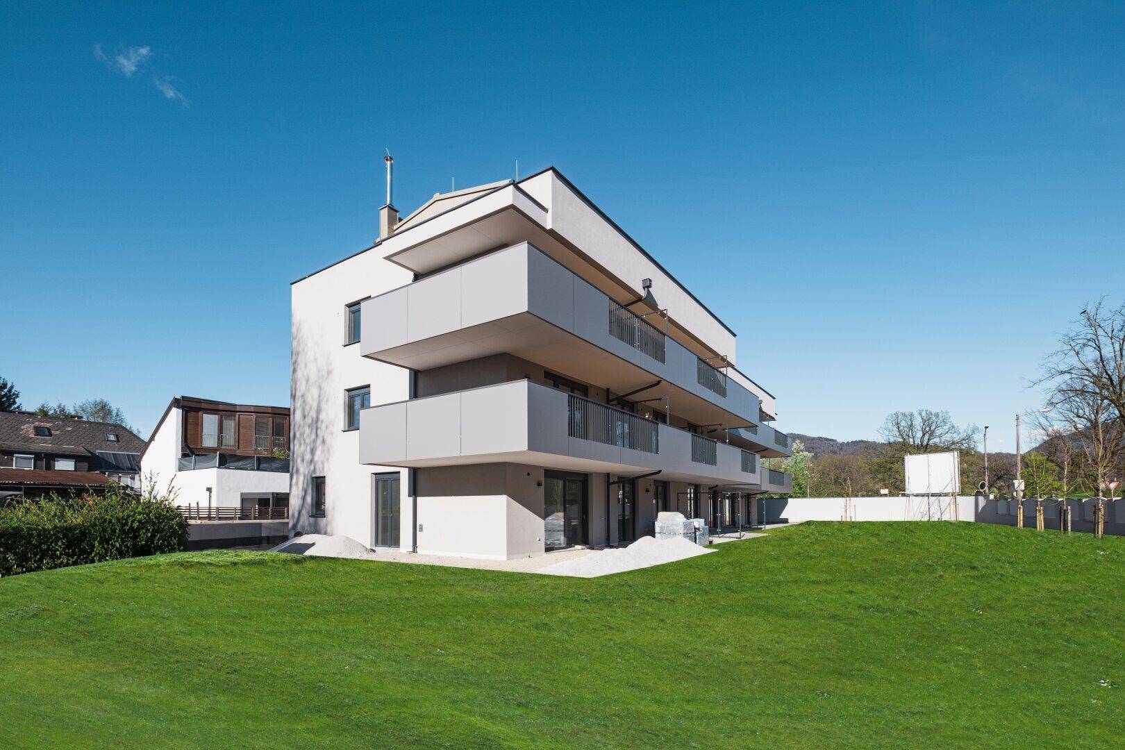 Moderner Neubau mit klaren Linien und Balkonen, umgeben von einer grünen Hügellandschaft.
