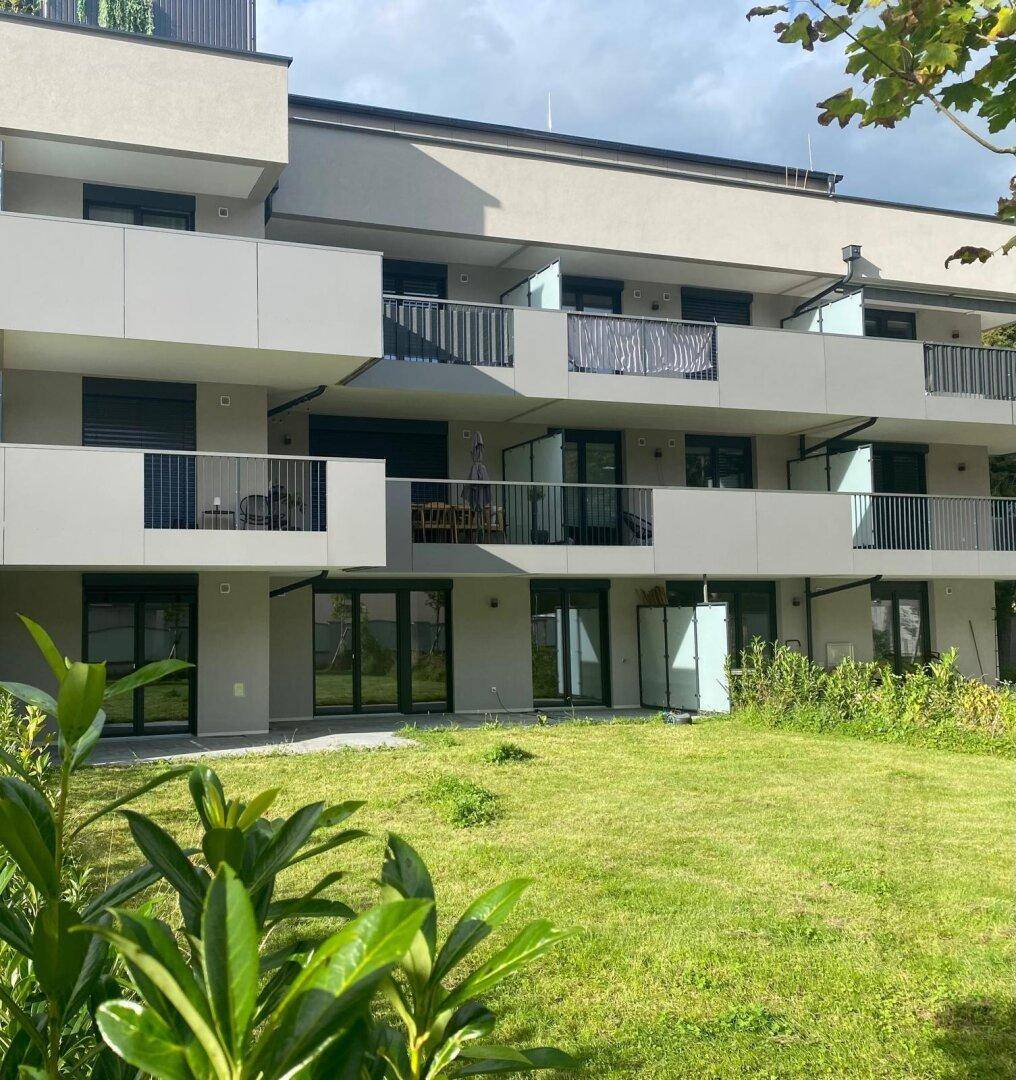 Neubau mit moderner Architektur, Balkonen und einer gepflegten Grünfläche im Vordergrund.
