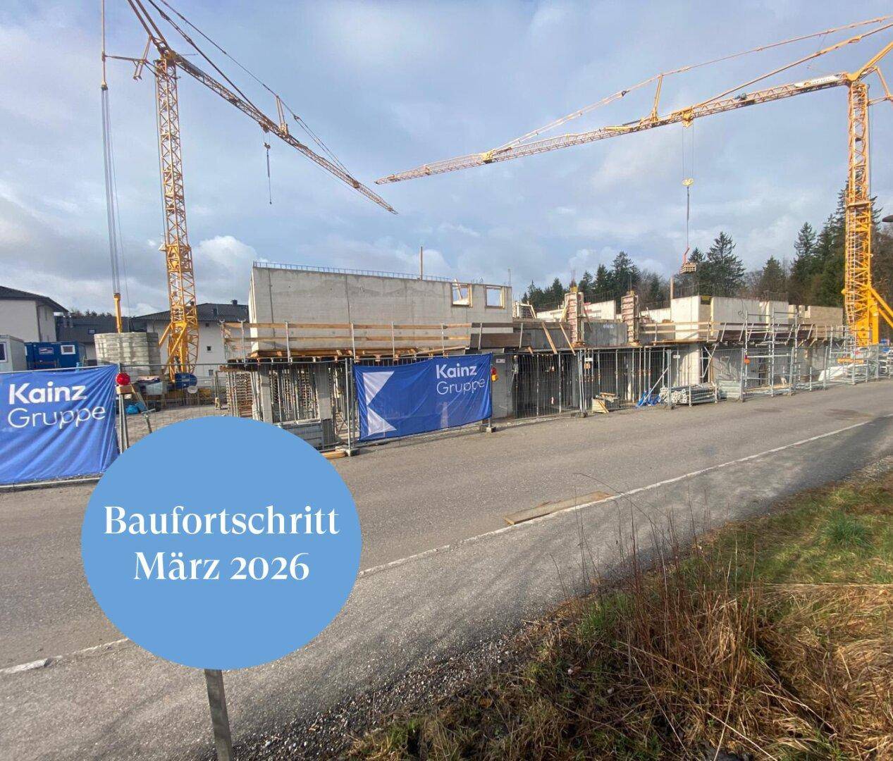 Baustelle mit Rohbauten entlang einer Straße und mehreren Baukränen im Hintergrund unter blauem Himmel.