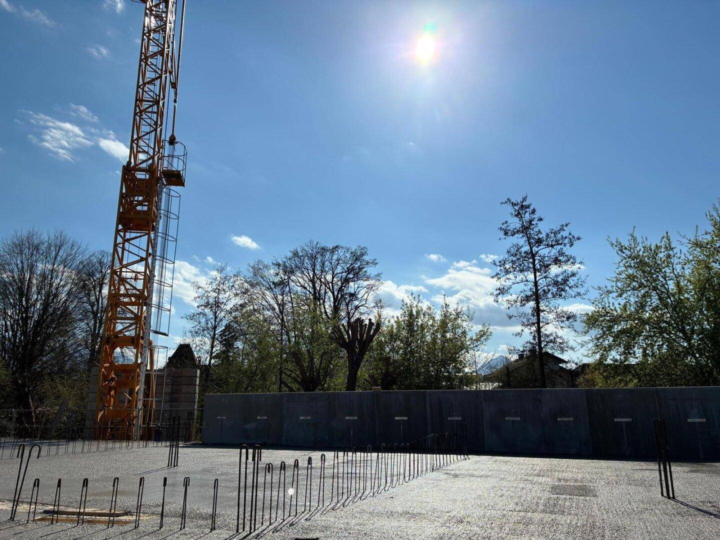 Baustelle mit Kran und Bewehrungsstahl für eine neue Betonplatte unter strahlendem Sonnenschein.