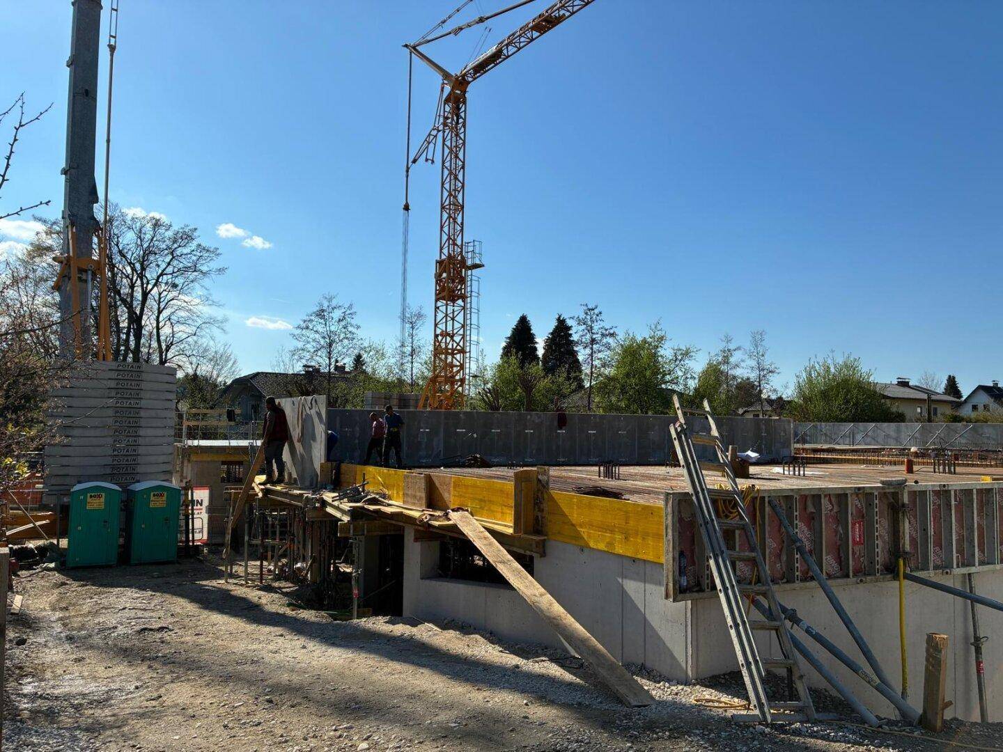 Fortgeschrittene Baustelle mit Schalung, Betonwänden und Kran, Arbeiter sind bei der Errichtung sichtbar.