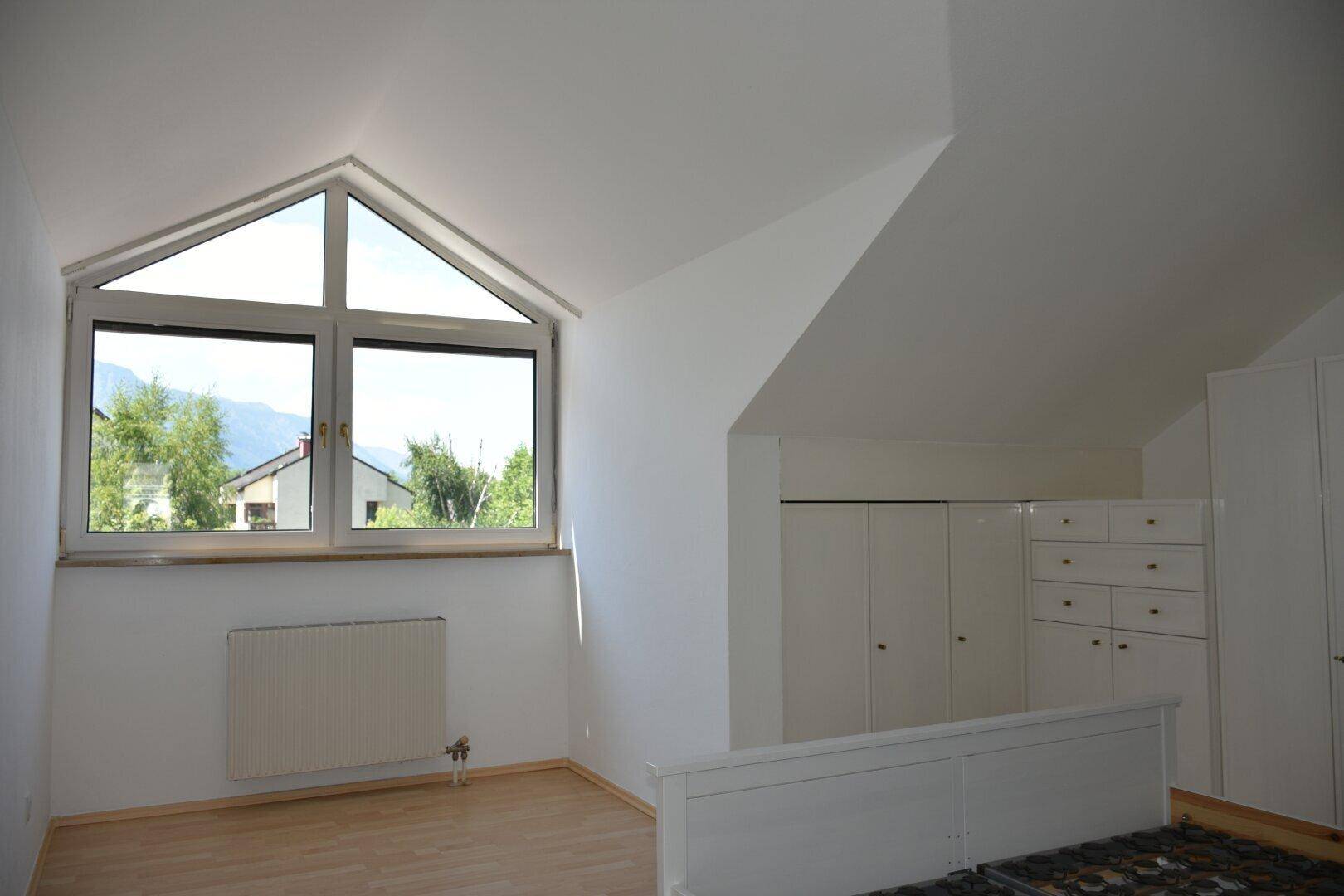 Schlafzimmer mit großem Giebelfenster, Dachschräge und Blick auf die umliegende Landschaft.