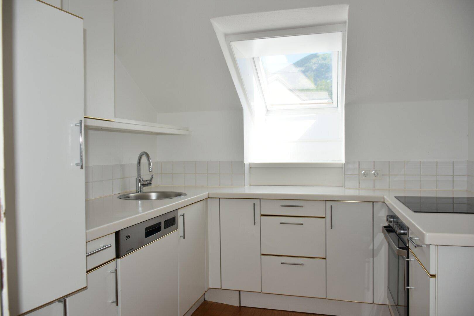 Helle Küche mit weißen Einbauschränken, modernen Geräten und einem Dachfenster für Tageslicht.