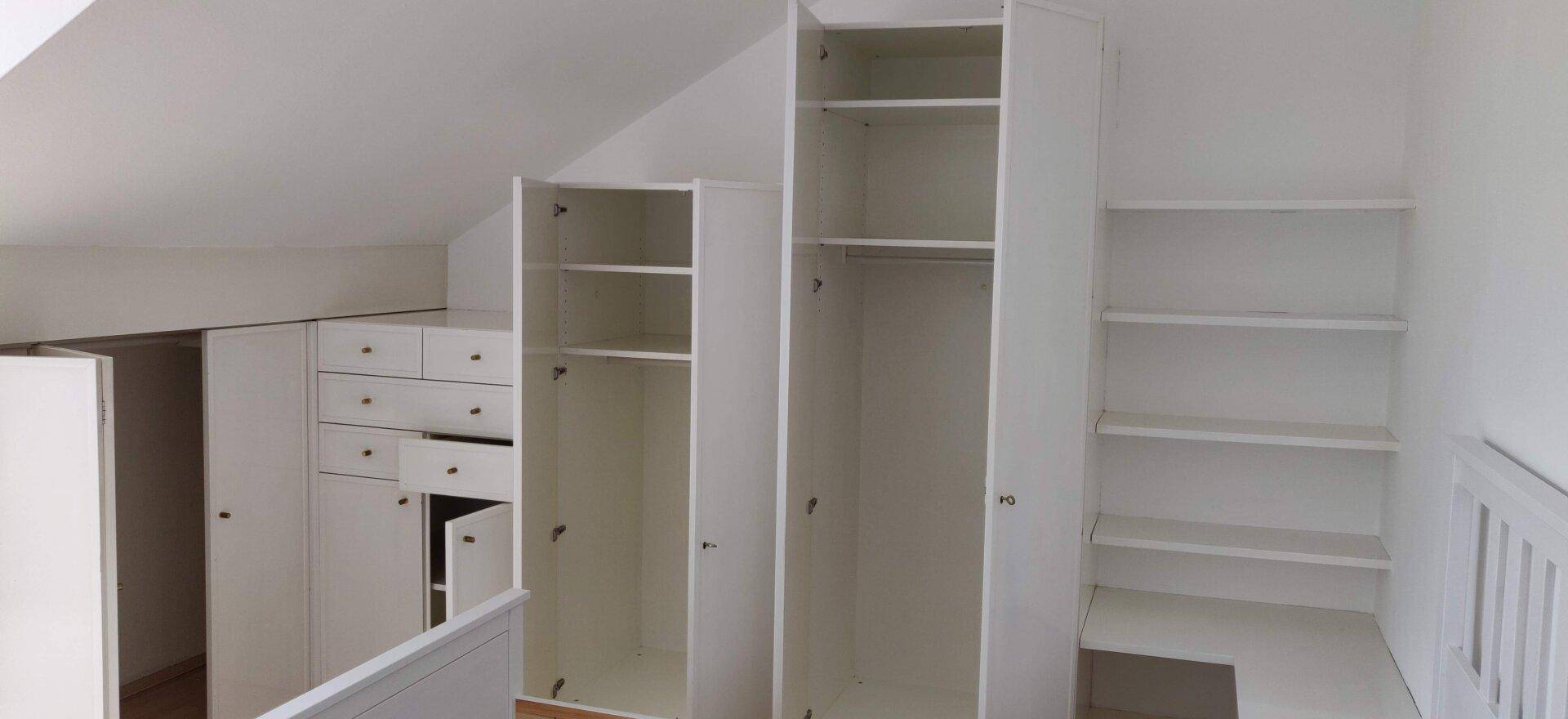 Schlafzimmer mit praktischen weißen Einbauschränken und Dachschrägen für optimalen Stauraum.