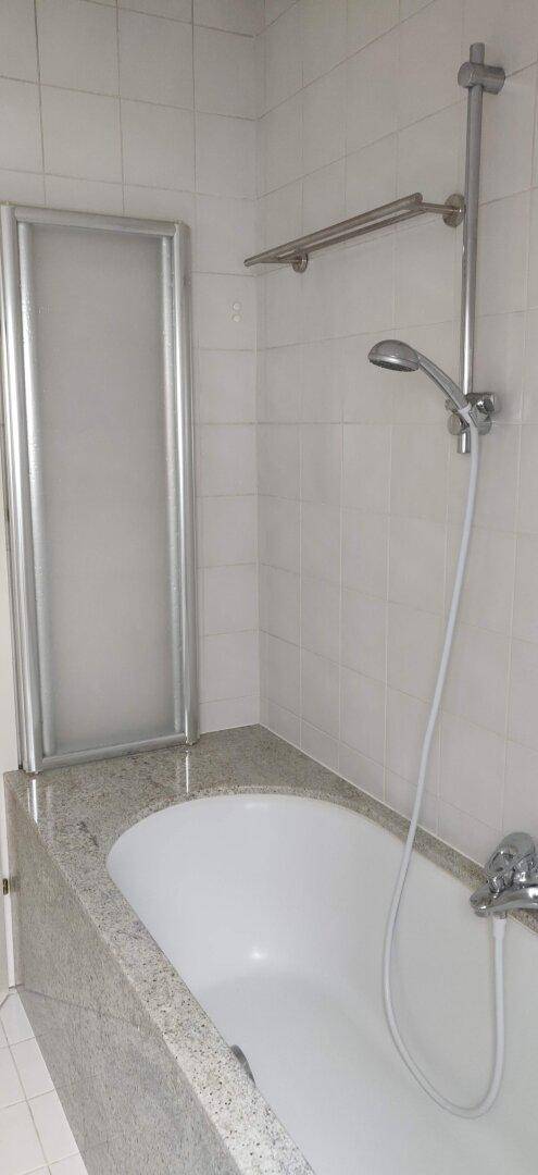Badezimmer mit Badewanne, Duschvorrichtung und hellen Fliesen an den Wänden.
