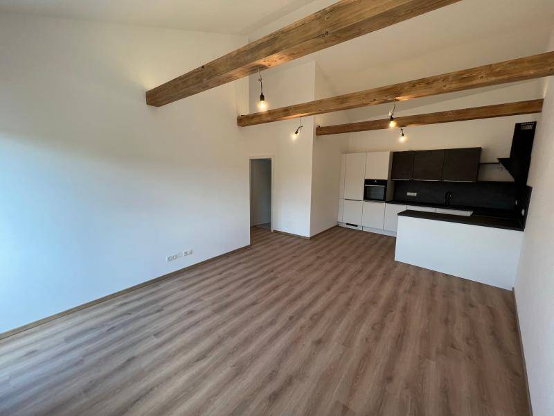 Offener Wohn- und Küchenbereich mit sichtbaren Holzbalken, Laminatboden und moderner Einbauküche.