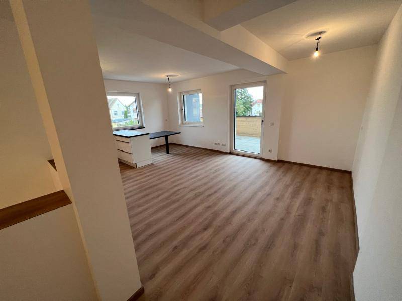 Geräumiger, heller Wohnbereich mit Laminatboden und Zugang zu einem Balkon durch eine große Glastür.