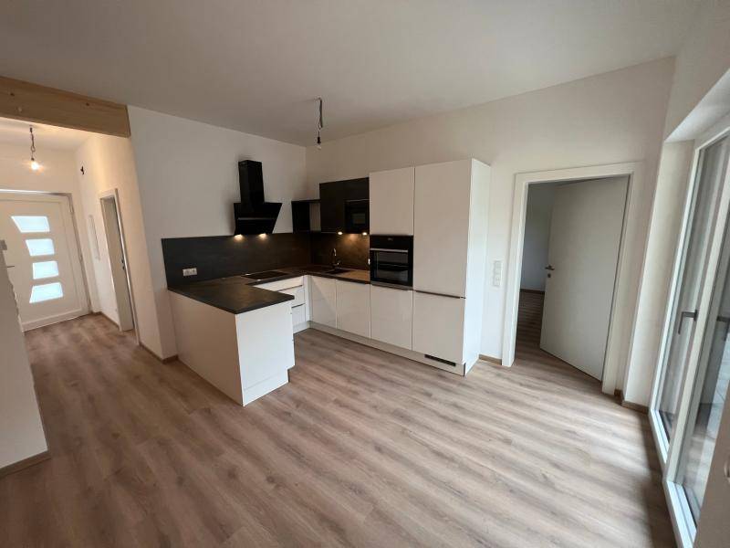 Moderne Einbauküche mit weißen Fronten, dunkler Arbeitsplatte und integrierten Geräten in offenem Wohnbereich.