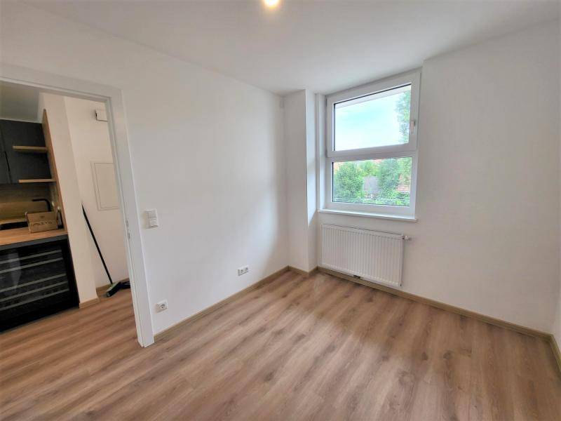 Helles Zimmer mit Laminatboden und Fenster mit Blick ins Grüne.